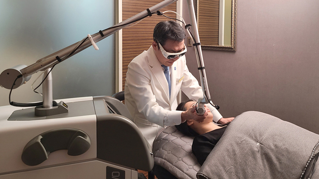 Practitioner wearing protective eyewear performing a facial laser treatment on a reclining patient at TAE Plastic Surgery Clinic.