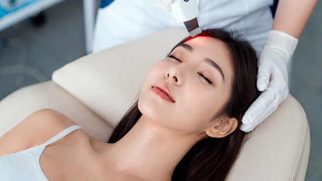 Practitioner using a handheld device on a woman’s forehead.