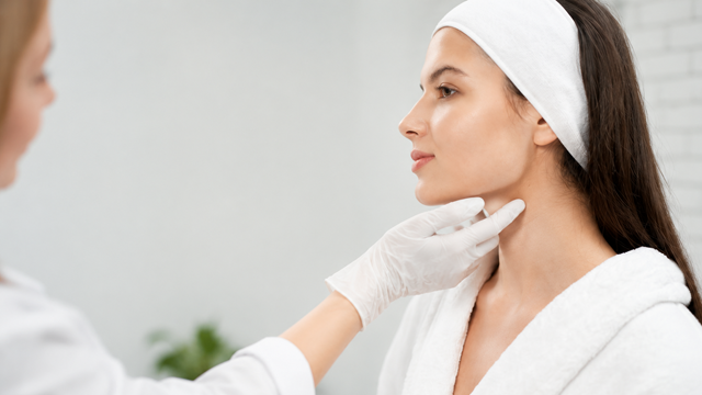 Practitioner wearing white gloves examining a woman’s chin and jawline.
