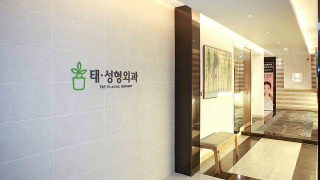 Hallway at TAE Plastic Surgery Clinic with clinic signage, framed artwork, and bench seating.