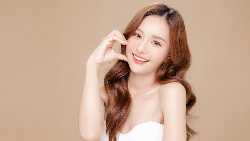 A smiling woman with smooth, even-toned skin posing against a neutral background, representing skin brightening, texture refinement, and youthful results achieved through advanced non-invasive laser rejuvenation treatments such as De Oro Dual Laser.