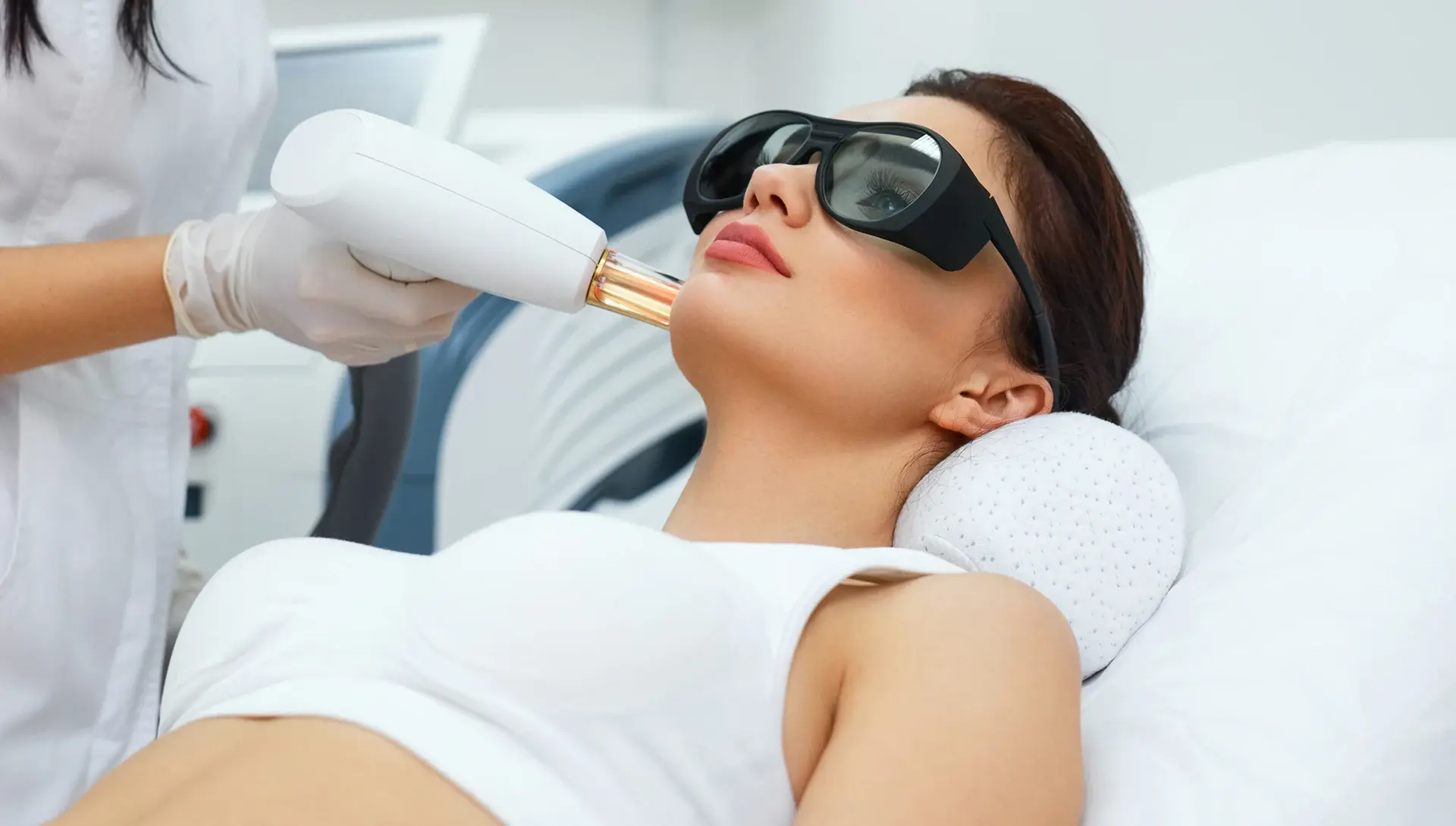 A patient wearing protective eyewear receives a non-invasive laser or energy-based facial treatment from a medical professional, representing advanced regenerative skin booster therapies offered in a clinical setting.
