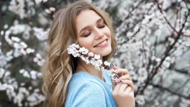 A woman with clear, glowing skin smiling gently while holding white blossoms outdoors, symbolizing natural skin renewal, cellular rejuvenation, and healthy skin achieved through advanced regenerative aesthetic treatments such as exosome skin boosters.