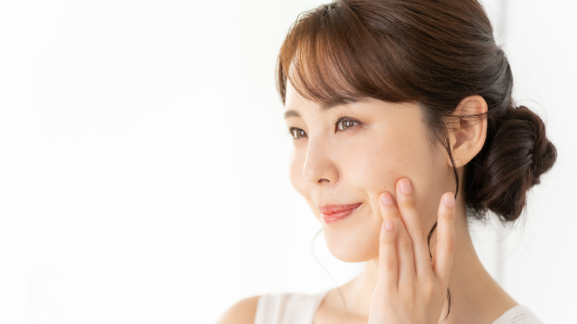 微笑的女性轻触脸颊,展现平滑肌肤与面部轮廓
