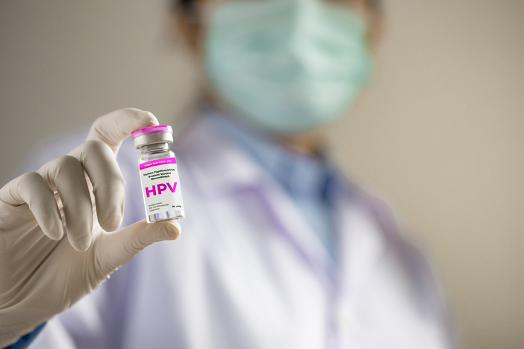 A healthcare professional wearing gloves and a mask holds a vial labeled “HPV,” representing clinically supervised HPV vaccination used for preventive protection against human papillomavirus infection.