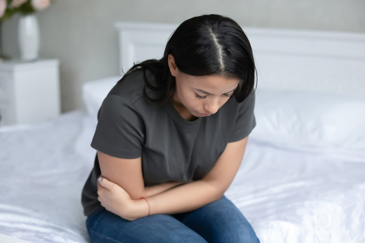 Woman sitting on bed experiencing discomfort related to chronic inflammatory conditions treatment care