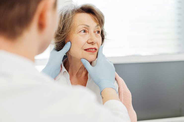 A clinician wearing gloves gently examines an older woman’s face during a consultation, representing personalized facial assessment and treatment planning for Botox or aesthetic care.
