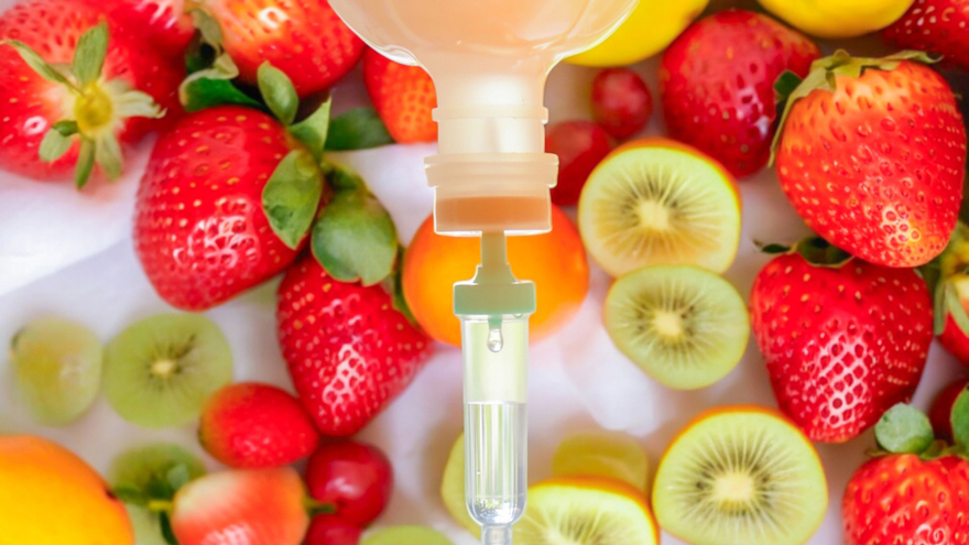 An IV drip bottle positioned above fresh fruits such as strawberries, kiwi, and citrus, symbolizing nutritional IV therapy that delivers vitamins, antioxidants, and hydration directly into the bloodstream for systemic wellness support.