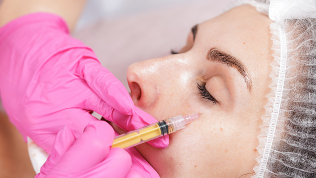 Practitioner wearing pink gloves administering an injection beneath a woman’s eye.