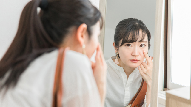 Woman looking in a mirror and touching the skin beneath her eye.
