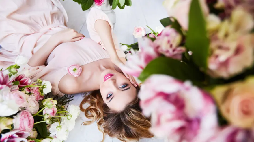 A woman with smooth, radiant skin lying among soft pink flowers, symbolizing skin tightening, texture refinement, and natural rejuvenation achieved through advanced energy-based treatments such as VirtueRF.