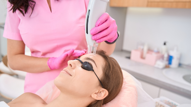 Fractional laser facial treatment — clinician applying a HALO or non-ablative fractional laser handpiece to a patient's forehead during a skin resurfacing session