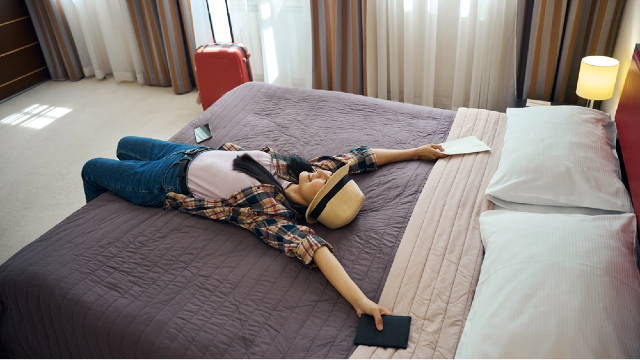 Jet-lagged woman collapsed on a hotel bed after arriving in Korea, showing why travel recovery needs to be planned around surgery